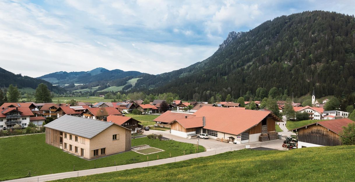 Eine malerische Landschaft mit traditionellen Gebäuden und Bergen im Hintergrund. Die Wiesen sind grün und die Atmosphäre ist friedlich.