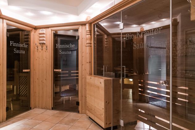 Ein entspannender Saunabereich mit Holzverkleidung und Glaswänden. Die Beschilderung zeigt die finnische Sauna und die Bio-Kräuter-Sauna.