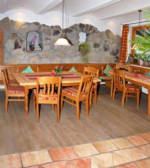 Ein gemütlicher Speisebereich mit Holzmöbeln und einem natürlichen Steinwand design. Die Tische sind liebevoll dekoriert und der Raum ist hell und einladend.