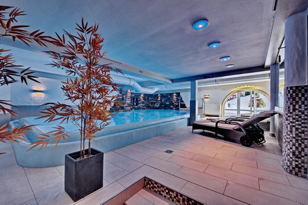 Ein eleganter Wellnessbereich mit einem blauen Schwimmbad und entspannenden Liegen. Die Atmosphäre ist beruhigend mit sanftem Licht und modernen Designelementen.