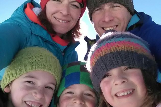 Eine Familie lächelt in die Kamera und trägt warme Winterkleidung. Sie stehen im Freien und scheinen Spaß zu haben.