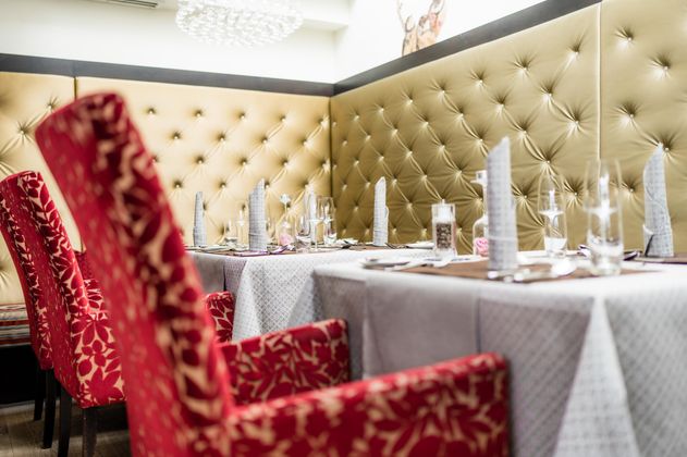 Ein elegantes Restaurant mit rot gepolsterten Stühlen und stilvollen Tischtüchern. Die Wände sind mit goldfarbenem, gepolstertem Material dekoriert.