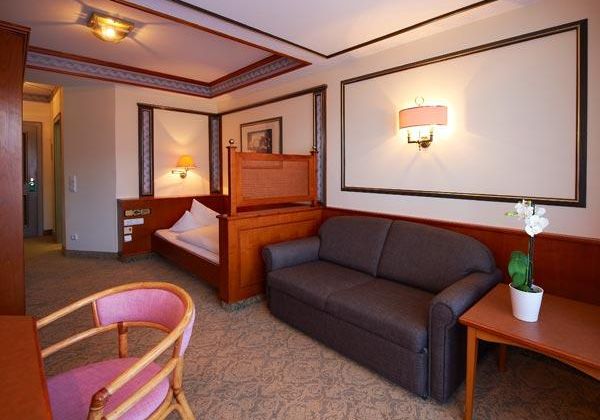 Ein gemütliches Hotelzimmer mit einem Sofa, einem Tisch und einem Stuhl. Die Wände sind in warmen Farben mit dekorativen Rahmen gestylt.
