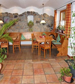 Ein gemütliches Restaurant mit Holztischen und bunten Vorhängen. Die Einrichtung ist von Pflanzen umgeben, was eine einladende Atmosphäre schafft.