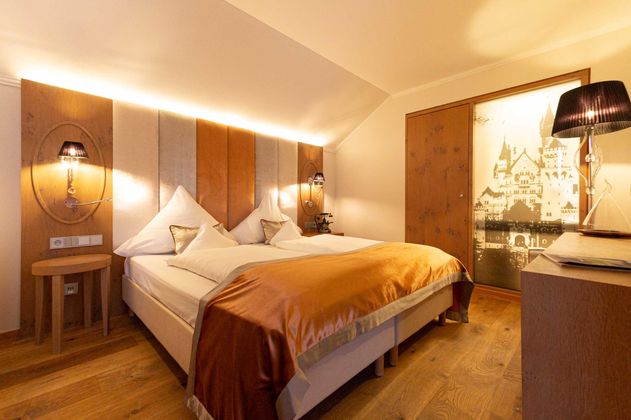 Ein gemütliches Hotelzimmer mit einem großen Doppelbett und warmen Holzdetails. Die Wände sind geschmackvoll gestaltet und eine Lampe sorgt für angenehmes Licht.