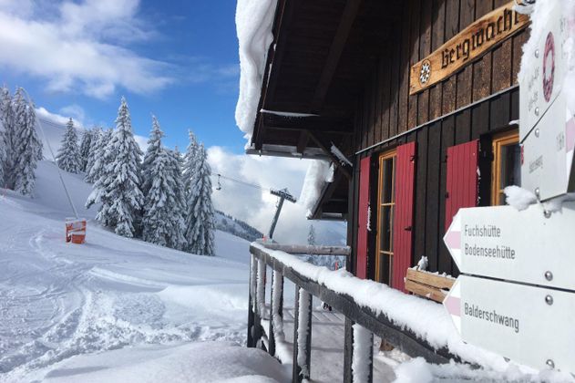 Verschneite Berghütte mit Schild "Bergmähdle", Wegweiser zu Berghütten und Balderschwang, Skilift im Hintergrund.