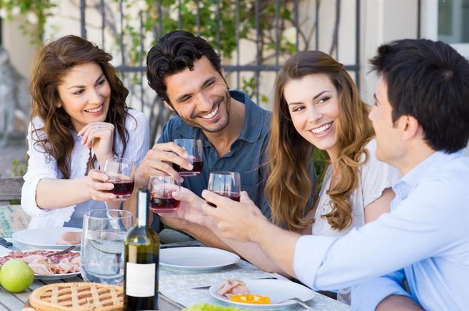 A group of four friends enjoys a joyful meal outdoors. They toast with glasses and laugh together.