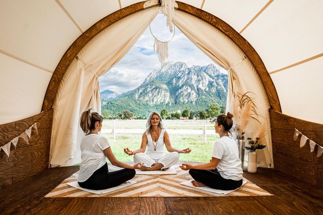 Eine Gruppe von Frauen meditiert in einem Zelt mit Blick auf majestätische Berge. Die Atmosphäre ist ruhig und entspannend, ideal für Yoga und Meditation.