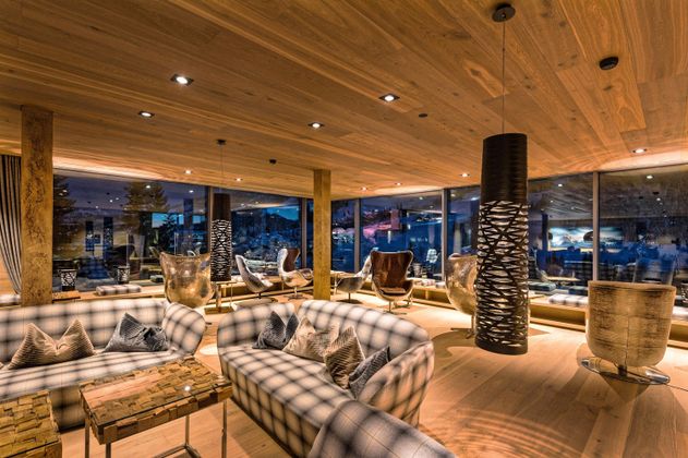 Ein modernes Lounge-Bereich mit Holzwänden und gemütlichen Möbeln. Große Fenster bieten einen Blick auf die Umgebung und schaffen eine einladende Atmosphäre.