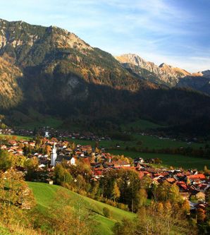 Eine malerische Alpenlandschaft mit einem kleinen Dorf im Tal. Umgeben von hohen Bergen und bunten Wäldern, strahlt die Szenerie Ruhe und Natürlichkeit aus.