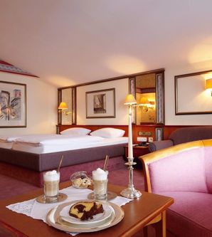 Ein gemütliches Hotelzimmer mit einem Doppelbett und einem bequemen Sessel. Auf dem Tisch stehen Getränke und ein Gericht zum Genießen.