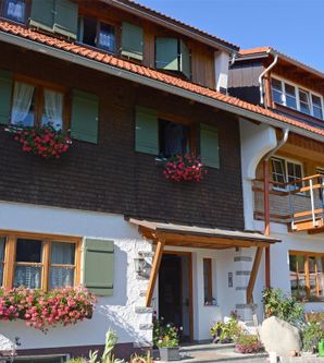 Ein schönes, traditionelles Haus mit grünen Fensterläden und blühenden Pflanzen. Der Himmel ist klar und die Atmosphäre ist einladend.
