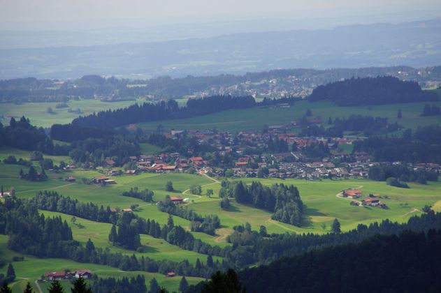 Eine malerische Landschaft mit sanften Hügeln und weitläufigen Wiesen. Im Hintergrund ist ein kleines Dorf mit Häusern zu sehen.